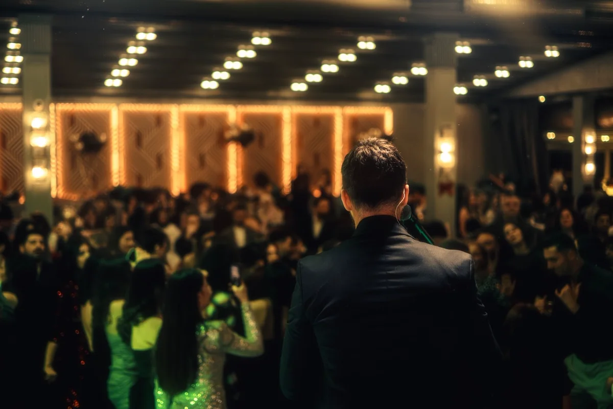 A host addressing a full ballroom under warm gold lighting at an evening awards event.
