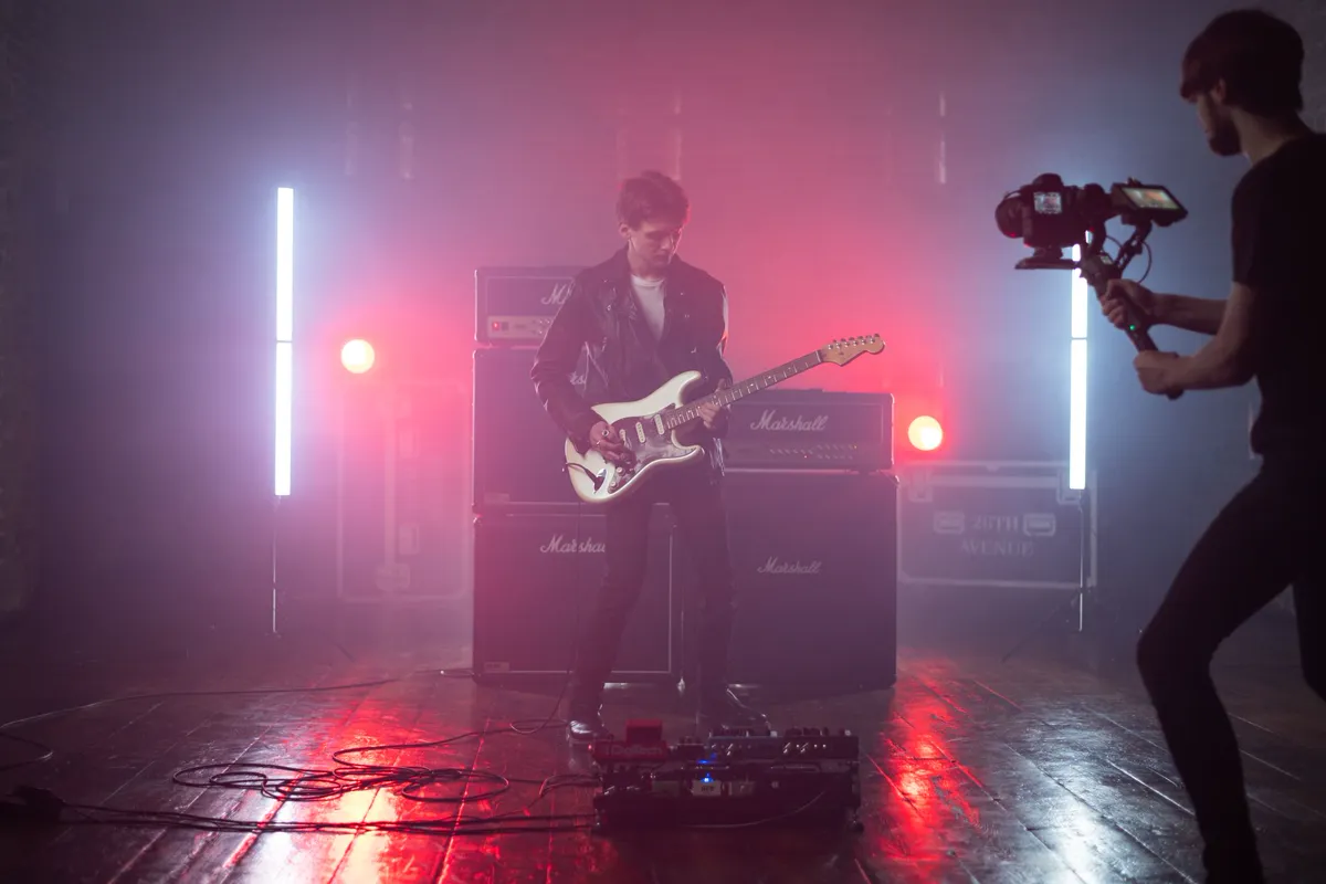 A musician performing under coloured stage haze while an operator films on a gimbal.